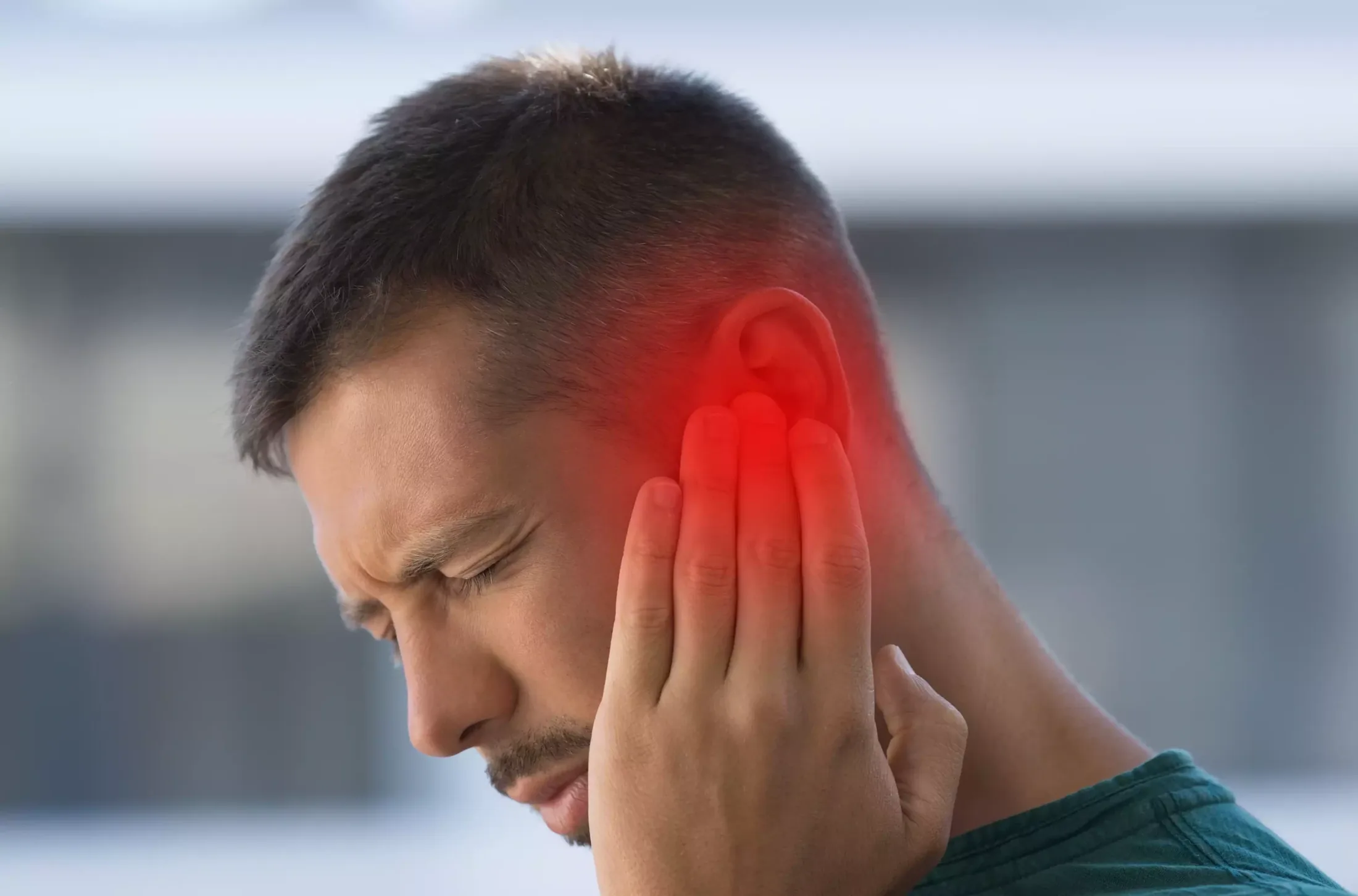 Homme grimaçant en se tenant l’oreille, douleur signalée en rouge