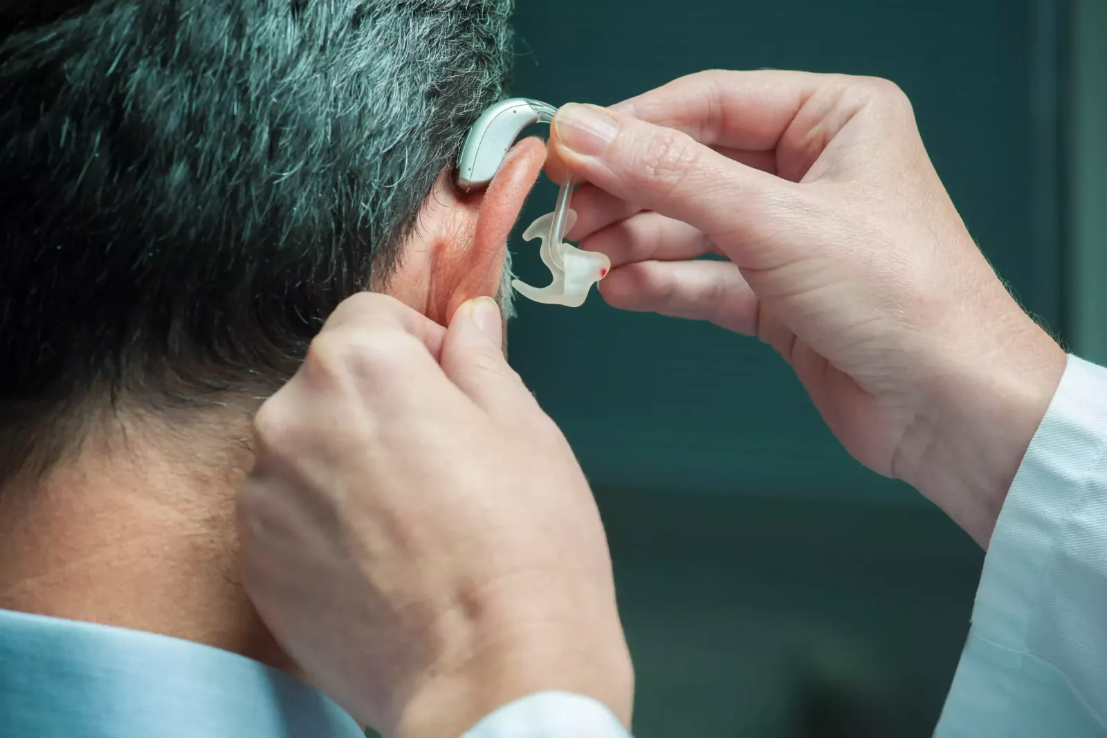 Audioprothésiste posant un appareil auditif derrière l’oreille d’un patient